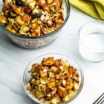 A glass bowl filled with Brussels sprouts hash with chunks of pancetta, Brussels sprouts, and potatoes.