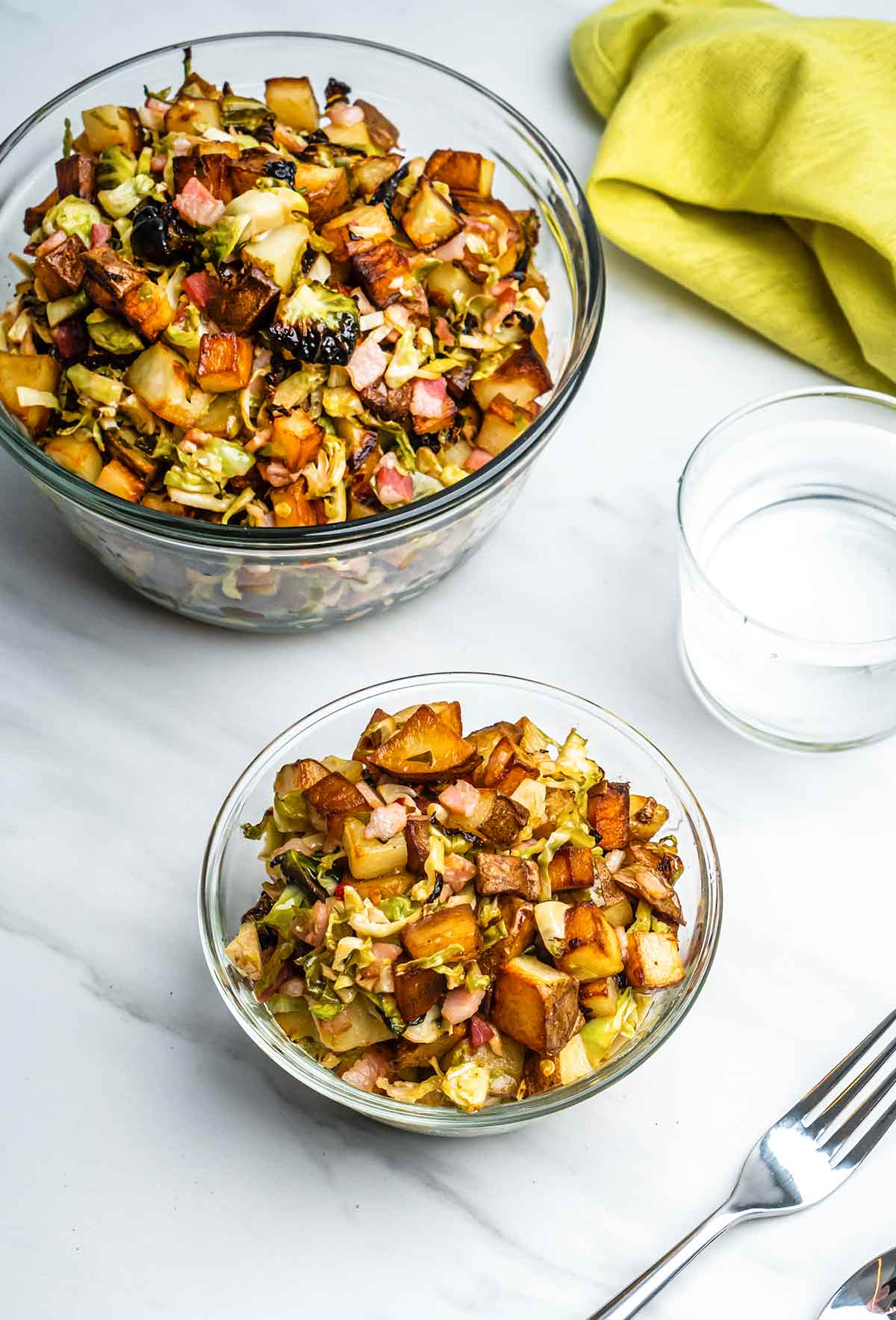 A glass bowl filled with Brussels sprouts hash with chunks of pancetta, Brussels sprouts, and potatoes.