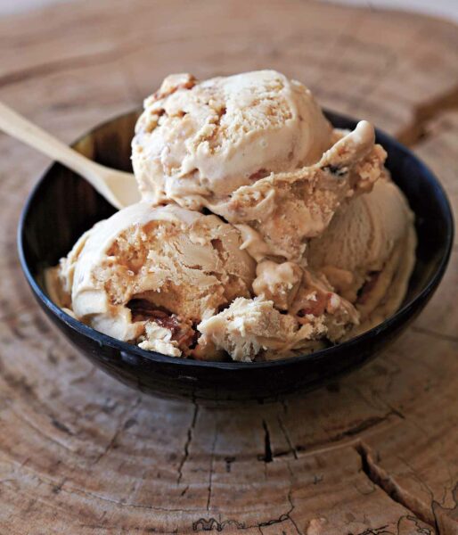 Butter pecan ice cream in a black bowl, with a spoon.