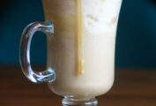 An Irish coffee mug filled with butterscotch beer with foam on top and a drizzle of butterscotch sauce.