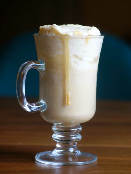 An Irish coffee mug filled with butterscotch beer with foam on top and a drizzle of butterscotch sauce.