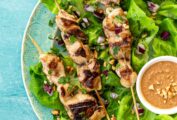 Citrus soy chicken skewers on a plate of lettuce, with a bowl of peanut dipping sauce.