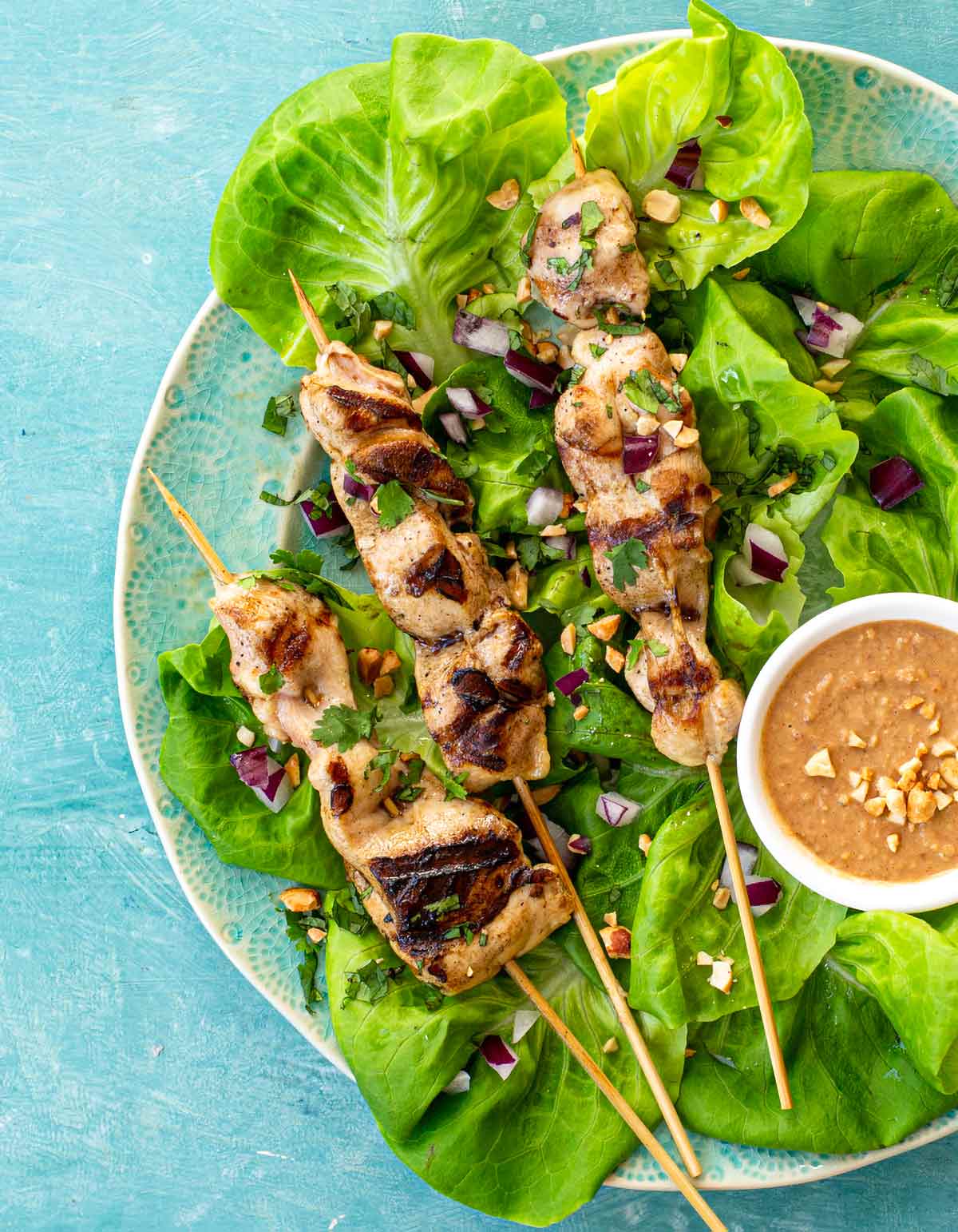 Citrus soy chicken skewers on a plate of lettuce, with a bowl of peanut dipping sauce.