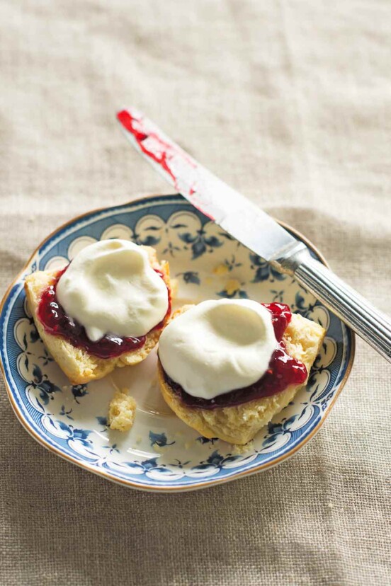 A blue and white saucer with a knife and 2 halves of a cream scone, topped with jam and whipped cream.