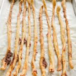 A baking sheet lined with parchment filled with 10 long, thin crispy cheese sticks.