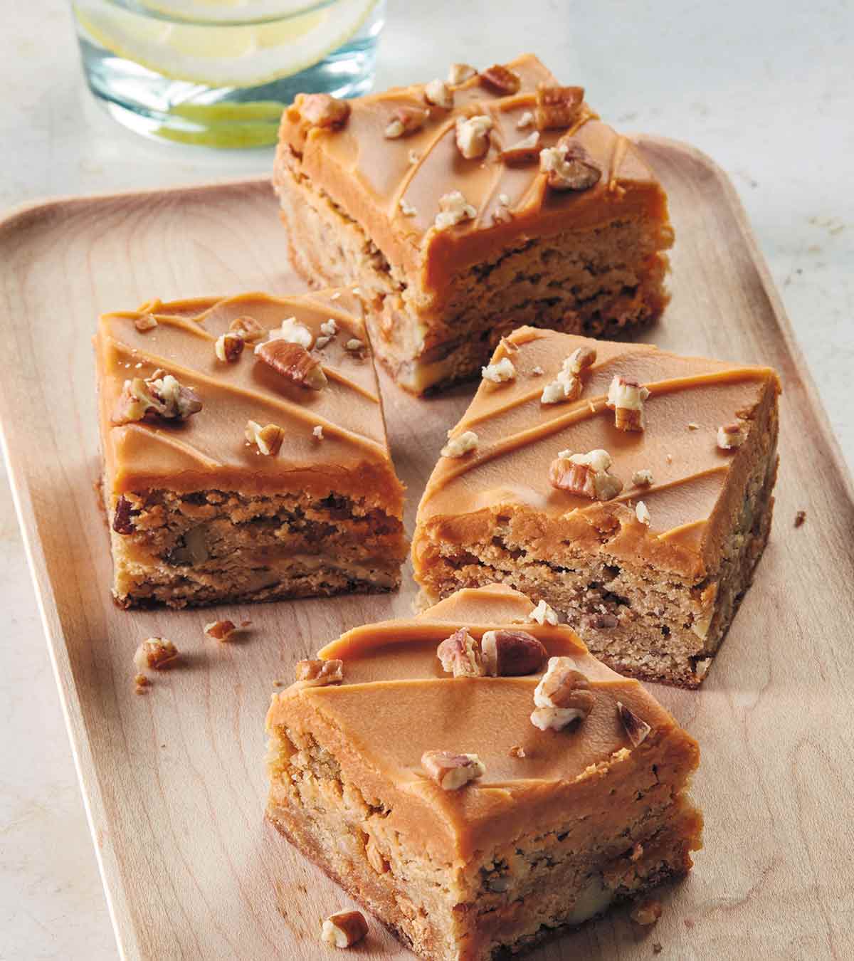 A wooden tray with 4 squares of double butterscotch blondies, with nuts sprinkled around them.