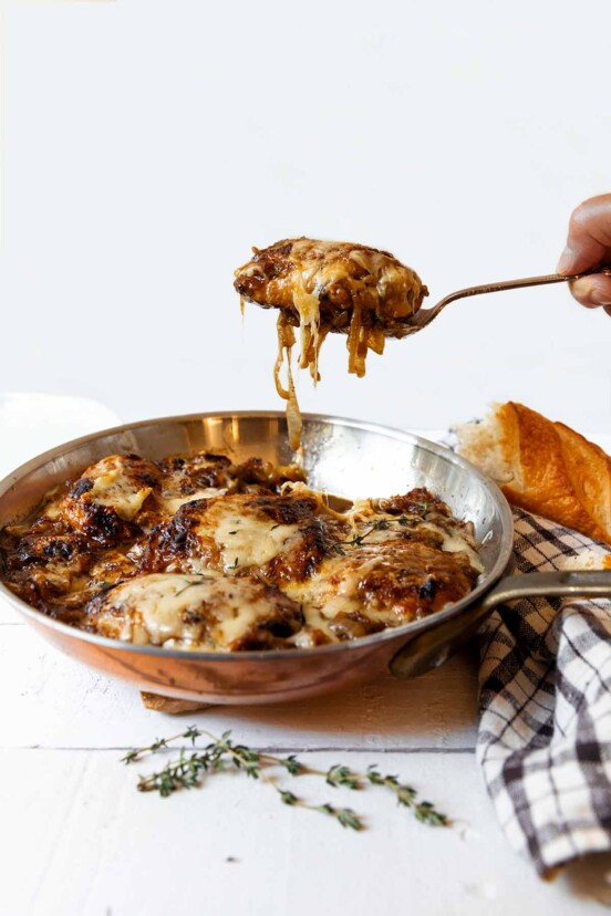 French onion skillet chicken in a copper frying pan with a person lifting out a serving