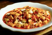Gnocchi with sausage and smoked mozzarella in a white bowl, with a stack of plates and cutlery behind.