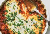 A white ribbed-edge tart pan filled with harissa baked eggs with goat cheese, with a spoon and topped with herbs.