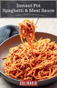 A pottery bowl filled with Instant Pot spaghetti with meat sauce, with a forkful of pasta.