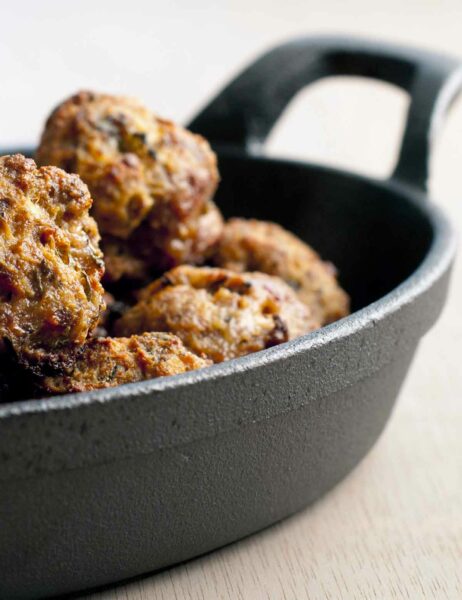 A cast-iron pan filled with koftinka meatballs on a white background.