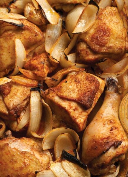 A close-up of a tray of Macedonian spiced chicken with pieces of chicken and onion slices.