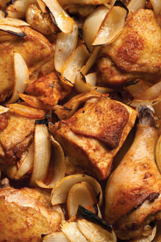 A close-up of a tray of Macedonian spiced chicken with pieces of chicken and onion slices.