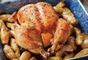 A blue enamel roast pan with a maple roast chicken, trussed and stuffed with lemon halves, sitting on a bed of fingerling potatoes.
