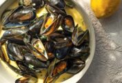 A white saucepan filled with mussels in a creamy white wine garlic sauce with lemons.