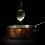 A spoonful of mustard cream sauce dripping in a copper pot