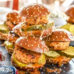 Nashville hot chicken sliders, piled up on a plate with sesame seeds and hot sauce.