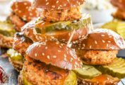 Nashville hot chicken sliders, piled up on a plate with sesame seeds and hot sauce.