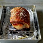 A pork loin roast, tied and seasoned with salt and pepper, on a foil-lined sheet pan with a wire rack.