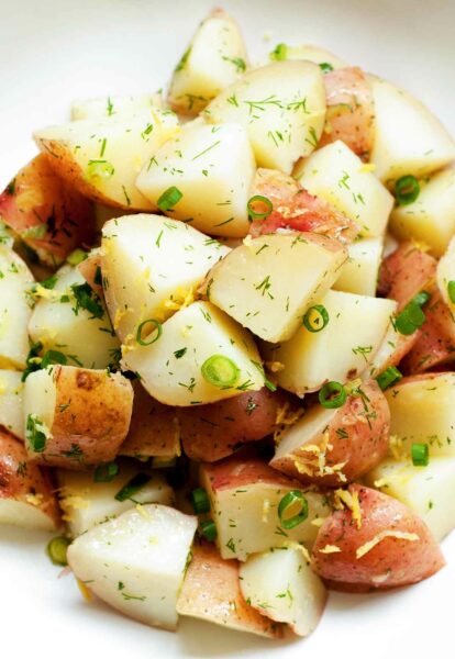A white bowl filled with potato salad with dill, including quartered red-skinned potatoes, tossed with dill, scallions, and lemon zest.