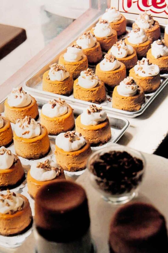 Pumpkin cheesecakes with gingersnap pecan crust on 2 sheet pans, topped with whipped cream and nuts.