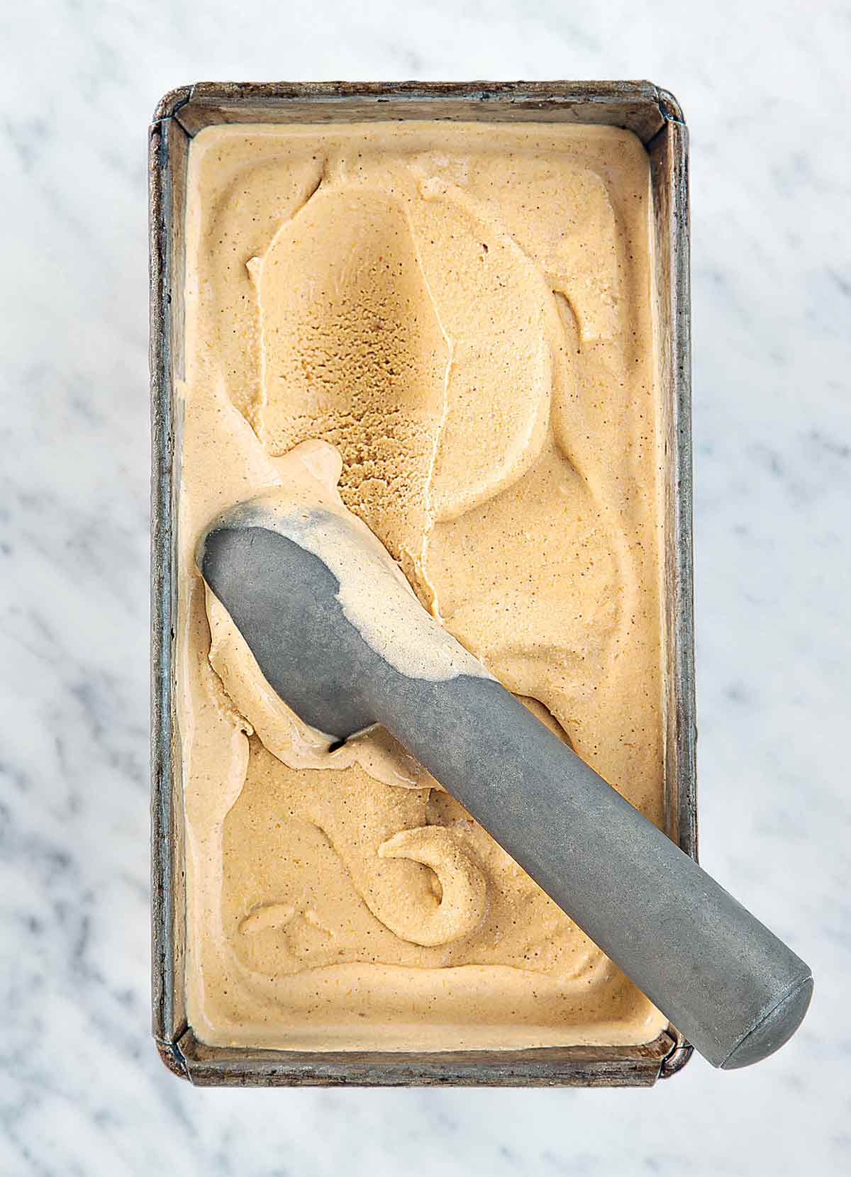 A metal container filled with pumpkin ice cream and a metal ice cream scoop resting inside.
