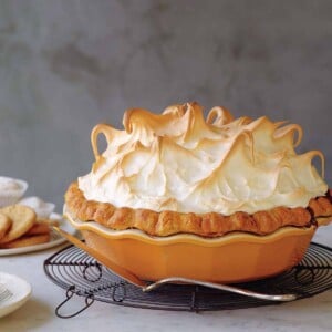 A pumpkin meringue pie in an orange stoneware pie plate, sitting on a cooling rack with a pie server.