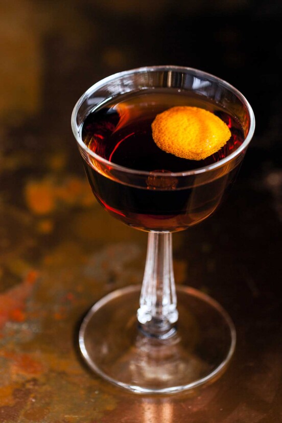 A coupe glass filled with a revolver cocktail, garnished with orange peel.