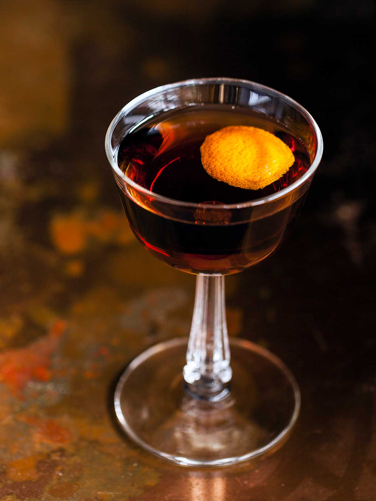 A coupe glass filled with a revolver cocktail, garnished with orange peel.