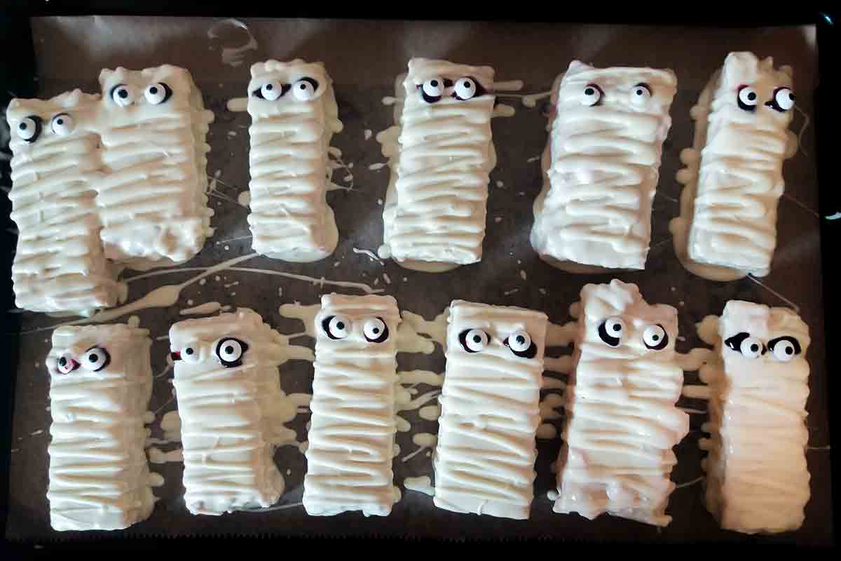 A baking tray with 12 Rice Krispie mummies, covered in white chocolate.