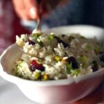 A white bowl with a hand taking a spoonful of rice pilaf with cherries and pistachios garnished with green onions.