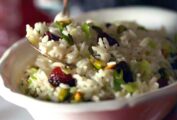 A white bowl with a hand taking a spoonful of rice pilaf with cherries and pistachios garnished with green onions.