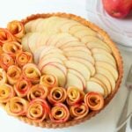 A apple rose tart on a glass cake stand.