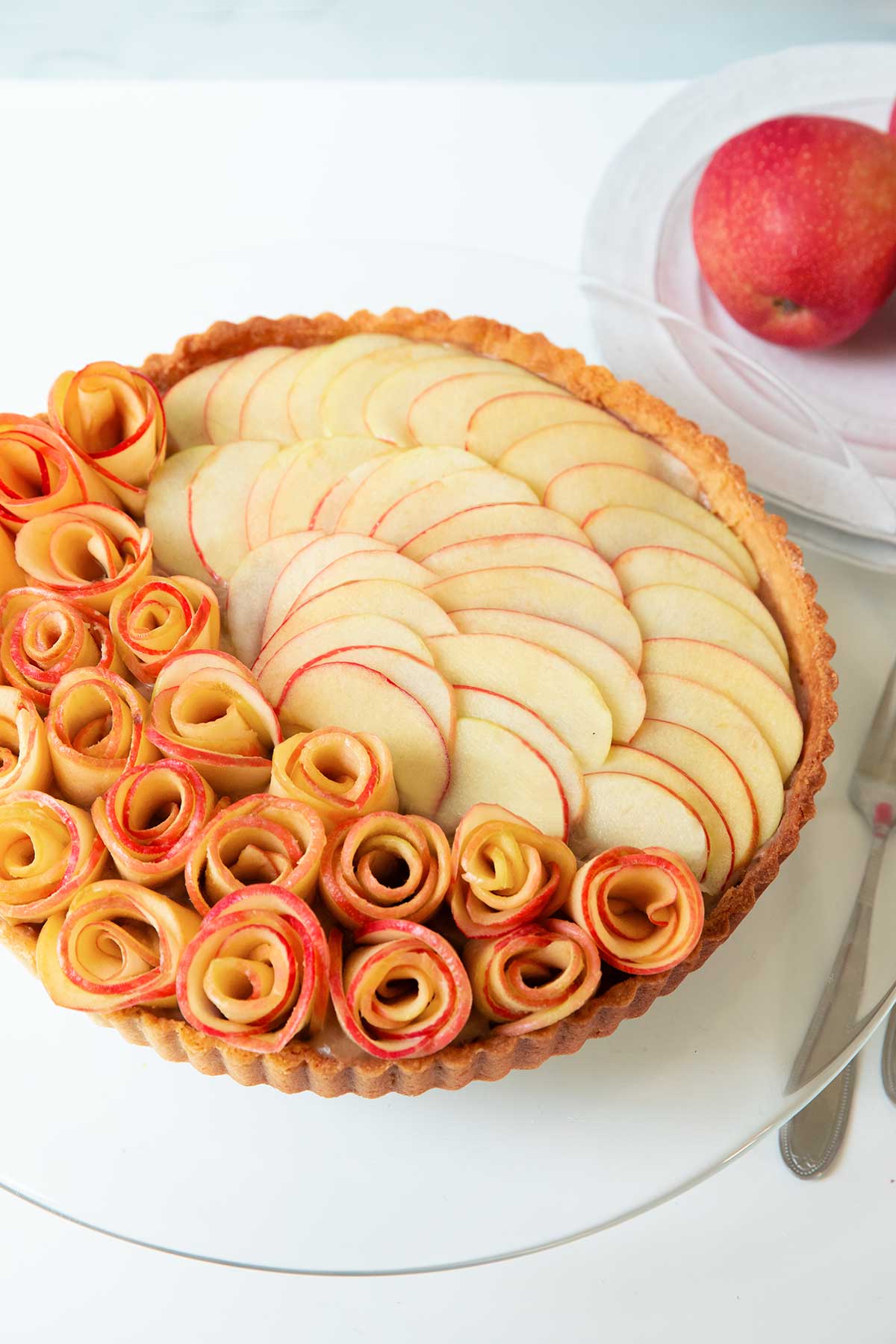 A apple rose tart on a glass cake stand.