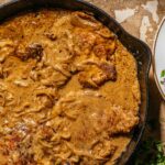 A cast-iron pan filled with smothered pork chops in a thick caramelized onion and cream sauce.