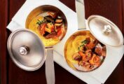 Soft polenta with forest mushrooms in two metal pots with lids.