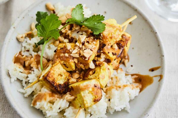 A white pottery bowl filled with tofu satay bowls garnished with cilantro and peanuts.