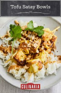 A white pottery bowl filled with tofu satay bowls garnished with cilantro and peanuts.