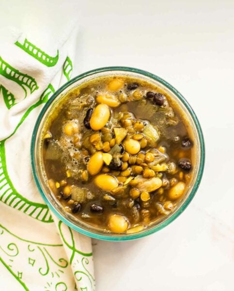 A green glass bowl of turmeric bean soup, filled with beans and broth, beside a green and white dish towel.