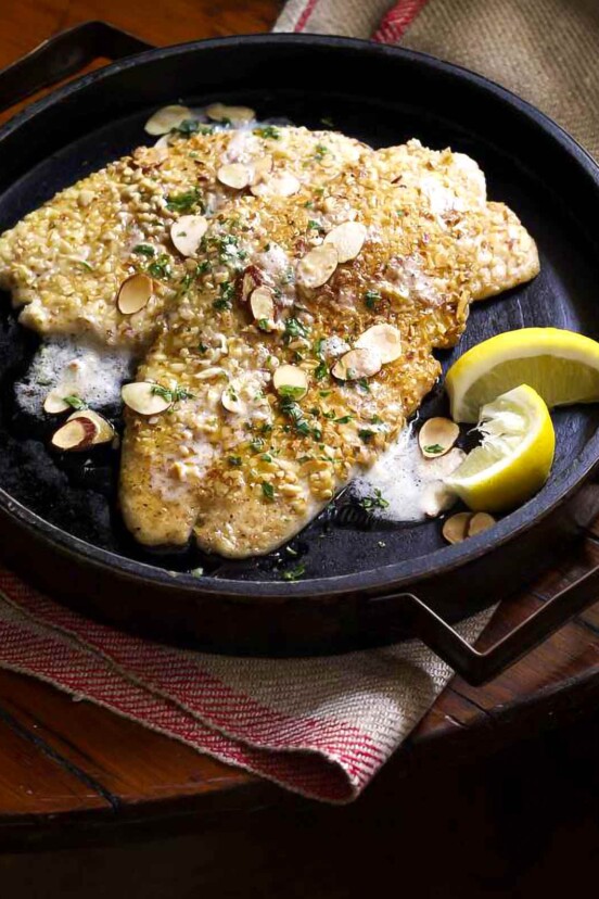 Almond flounder meunière in a wooden serving dish topped with sliced almonds and lemon wedges on the side.
