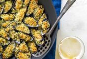 Baked mussels with breadcrumbs in a cast-iron pan with a serving spoon, on a blue tablecloth.