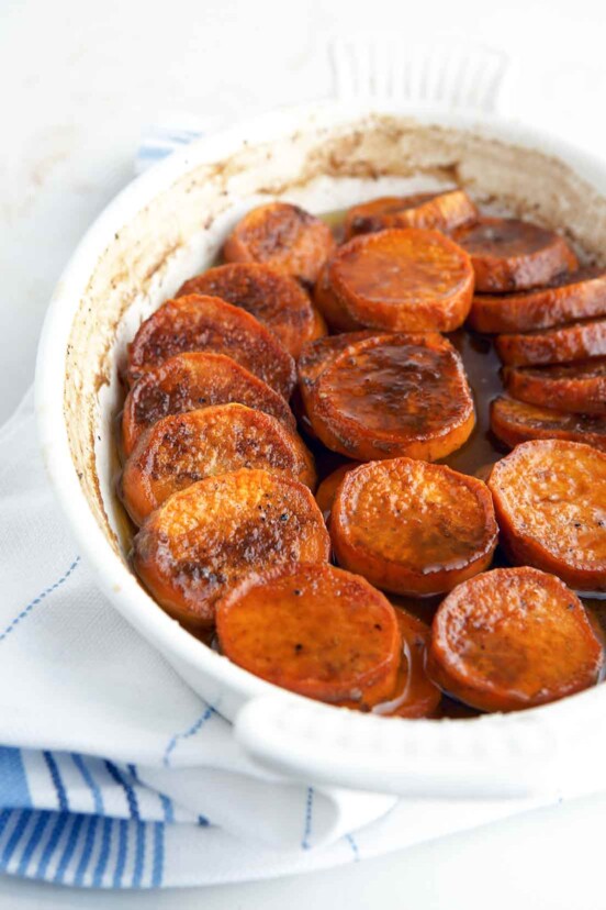 Bourbon sweet potatoes in a white oval baking dish, sitting on a white and blue tea towel.
