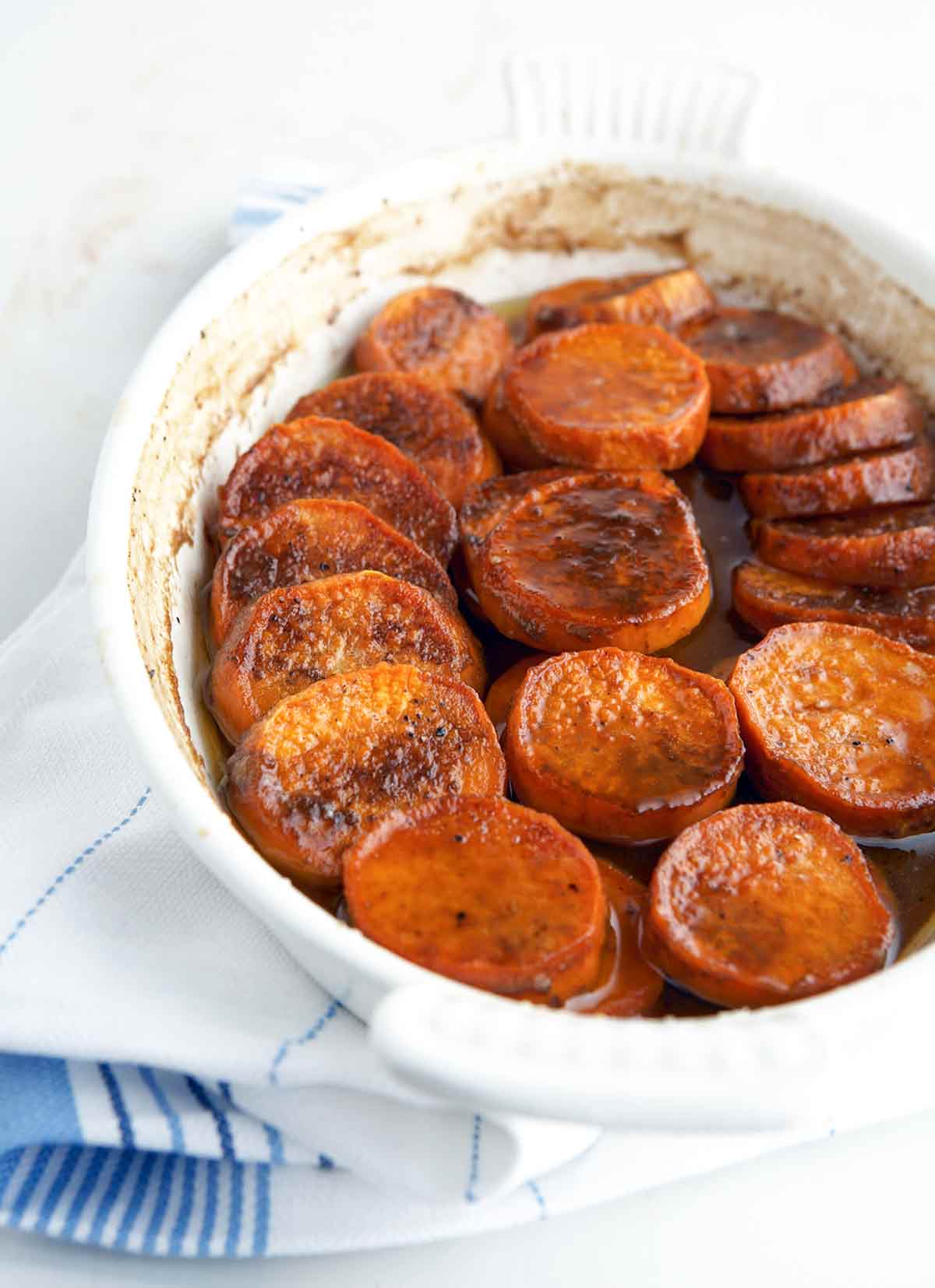 Bourbon sweet potatoes in a white oval baking dish, sitting on a white and blue tea towel.
