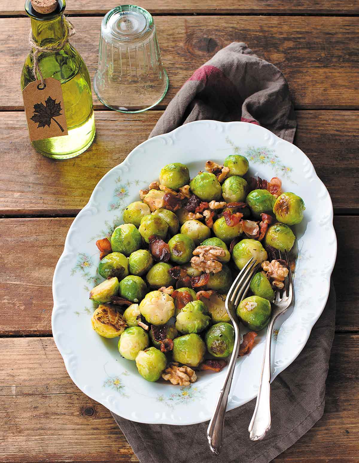 Brussels Sprouts with Walnuts and Pancetta on a large white floral platter with 2 serving forks.