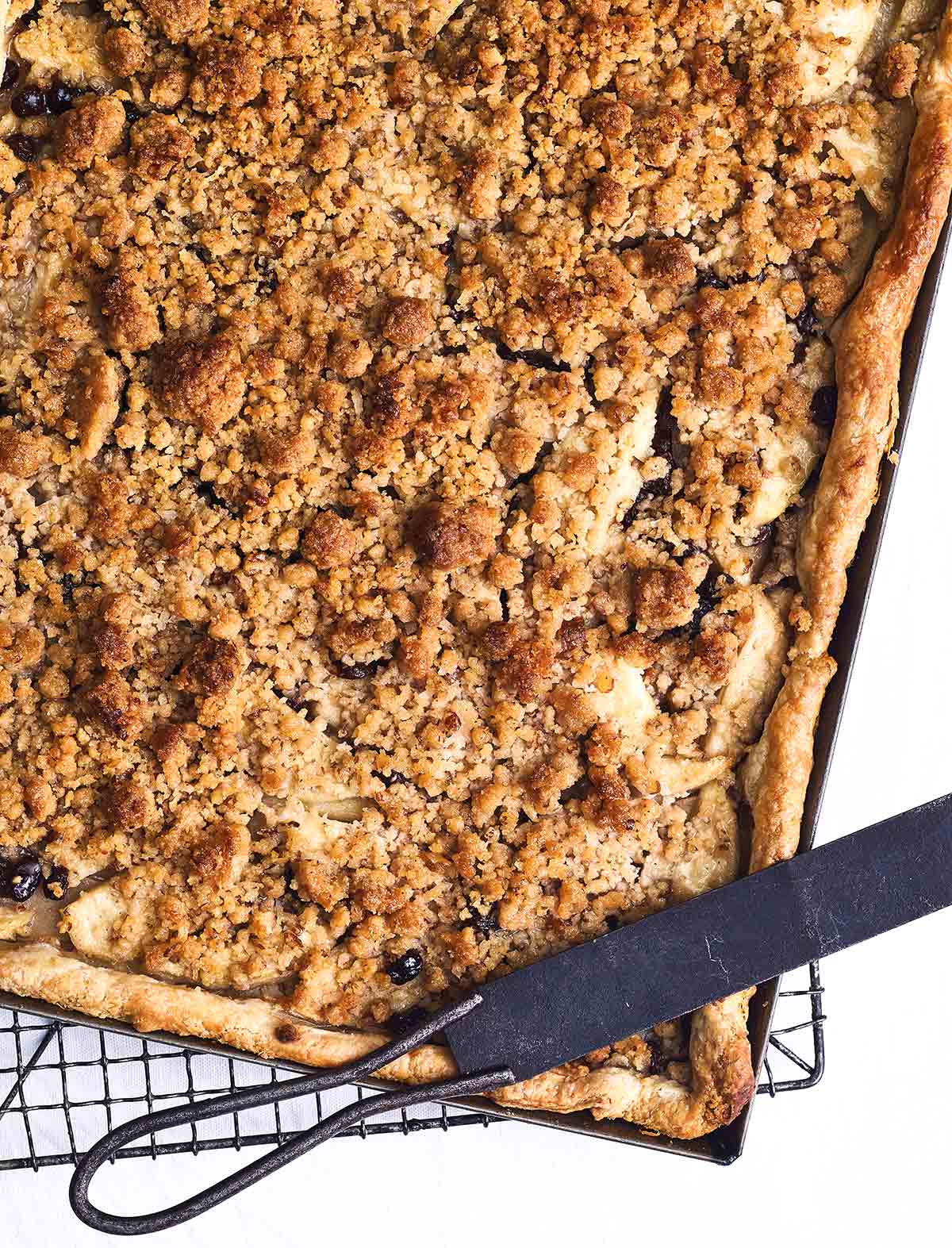 Caramel apple slab pie in a large metal sheet pan, on a wire rack with a pie knife.