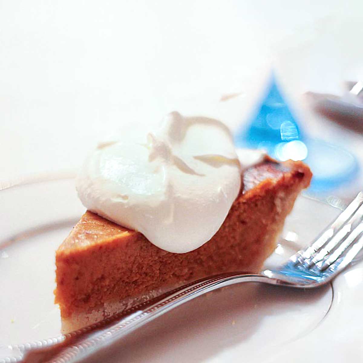 A slice of caramelized butternut squash pie with a dollop of whipped cream on a plate with a fork.