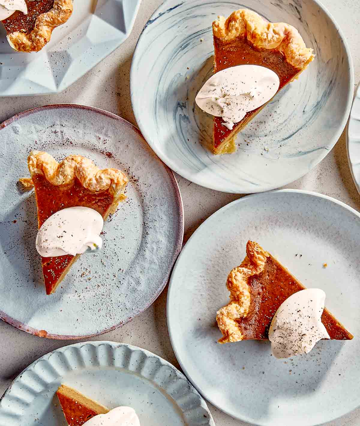 Caramelized honey pumpkin pie in slices on dessert plates, each garnished with dollops of whipped cream and pumpkin pie spice.