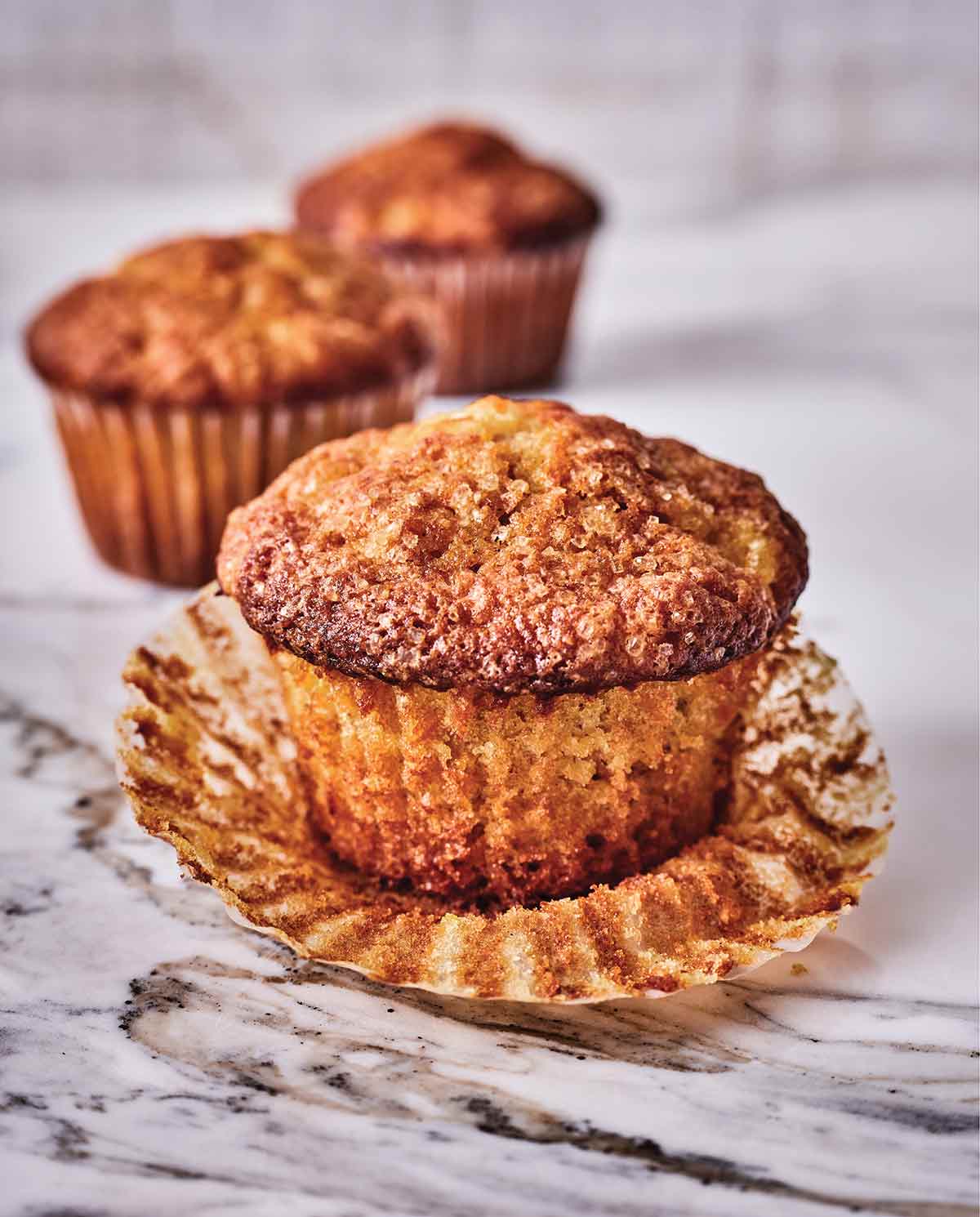 Carrot, pineapple, and candied ginger muffins on a counter, the one in front has its liner peeled off.