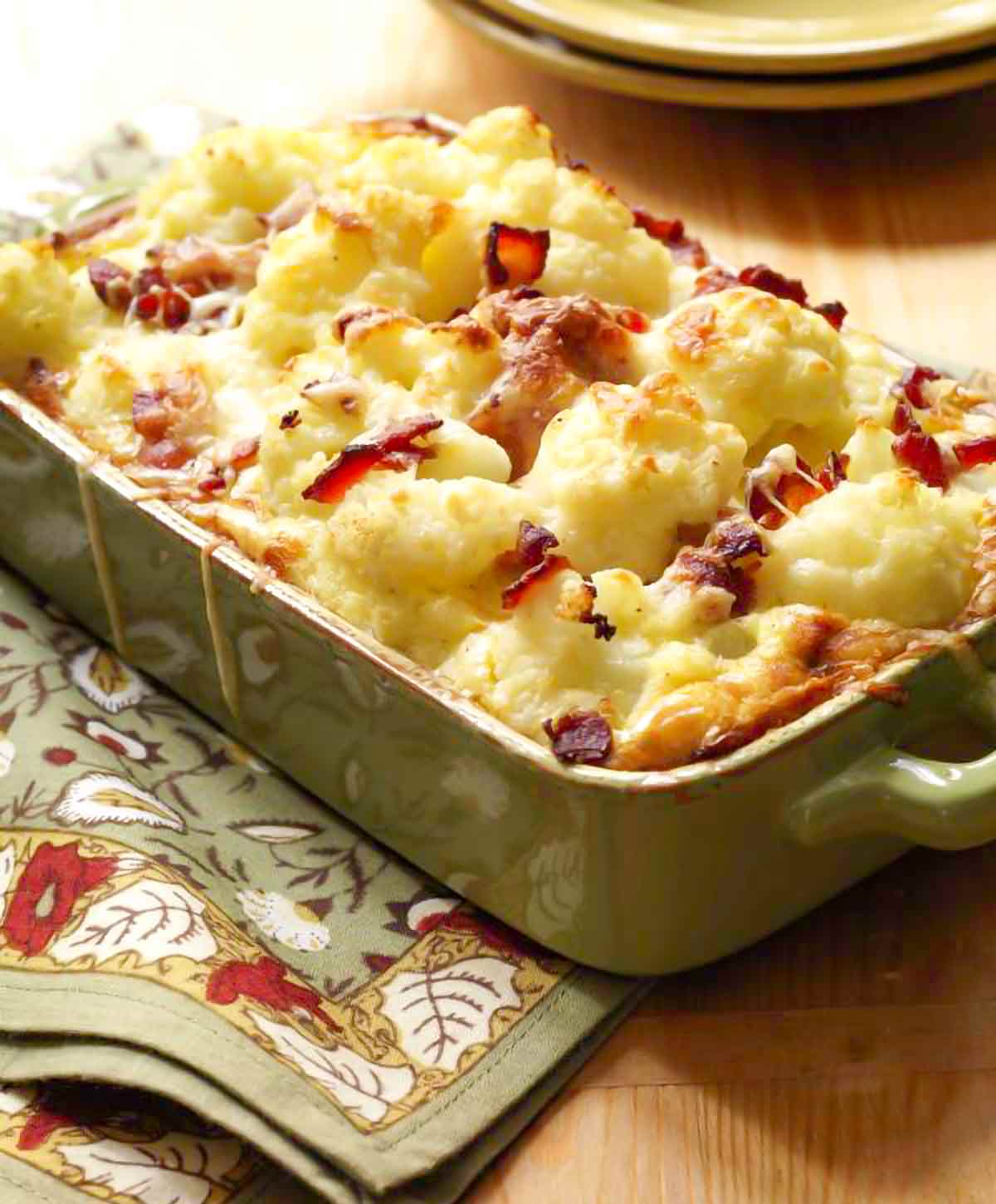Cauliflower bacon gratin in a large green rectangular baking dish with melted cheese.