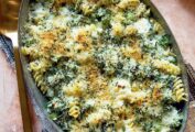 Baked cheesy pasta with broccoli in a large metal casserole dish, with a serving spoon and napkin.